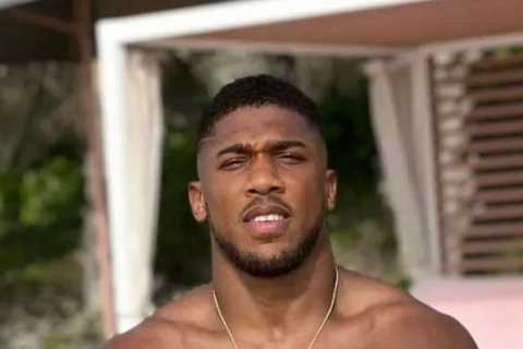 Anthony Joshua shows off shredded physique and looks ready for battle while sitting on beach ahead..